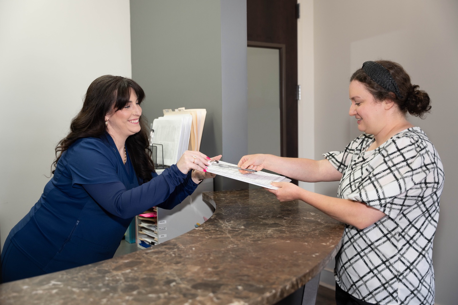A dental assistant gives a clipboard form to sign